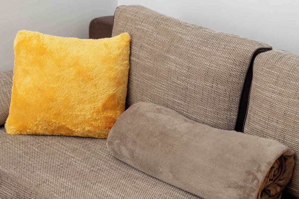 A close-up of a sofa with a yellow cushion in the living area. It emphasizes the cozy and colorful touches in the apartment’s interior.