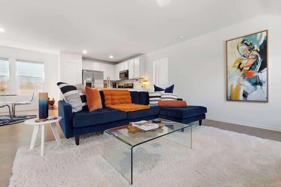 Spacious living room with a cozy navy sectional, bright natural light, and a 55” TV for streaming your favorite shows. This open-concept space flows into the kitchen and dining areas, creating the perfect place to unwind, gather, and relax.