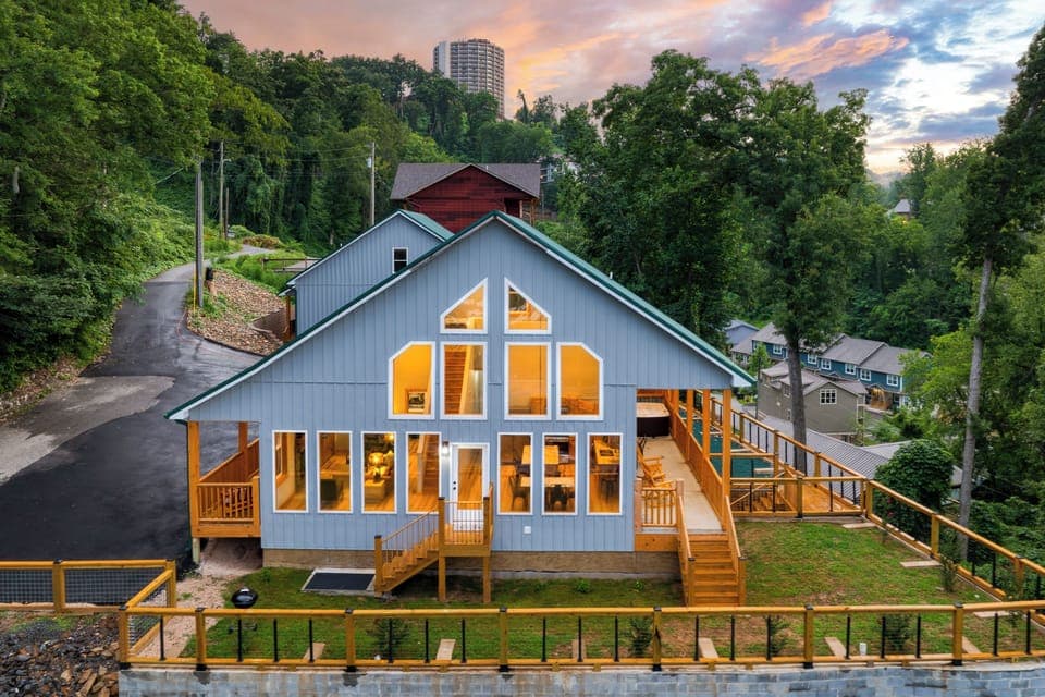 Warm sunset glow over this modern mountain home, featuring expansive windows, wraparound decks, and a peaceful wooded hillside setting. (Perfect Too)