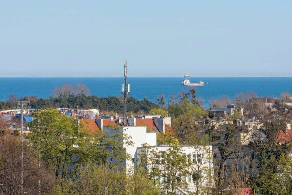 A distant view of the sea beyond a city area with buildings and greenery. The horizon line is clearly visible under a bright sky.