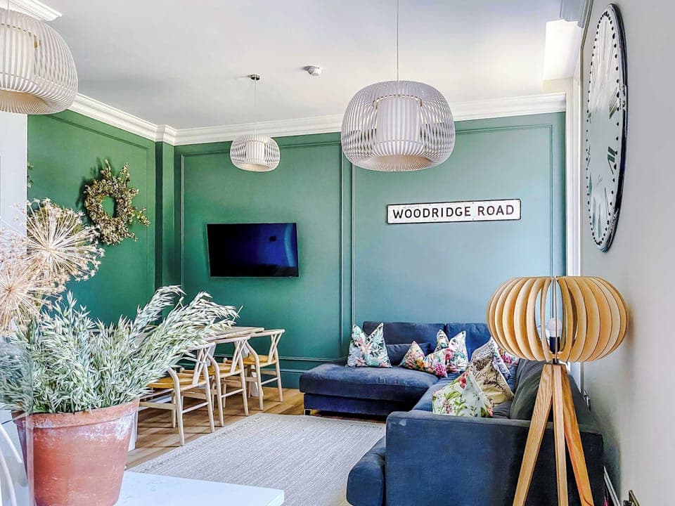 Stylish and inviting living space with elegant green panelled walls, warm wood floors, and modern décor. Relax on the plush corner sofa, enjoy the wall-mounted TV, or dine in comfort. A cosy yet sophisticated setting perfect for both business and lei