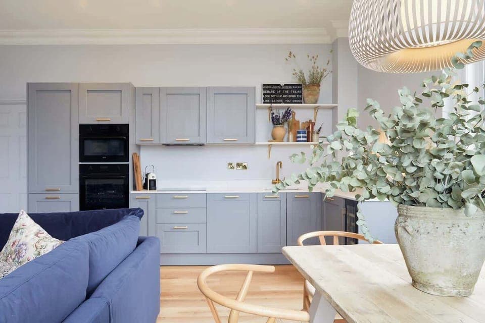 A welcoming living area with navy sectional, decorative pillows, and mounted TV. Elegant panel molding, wreath accent, and natural light from plantation shutters create a warm retreat.