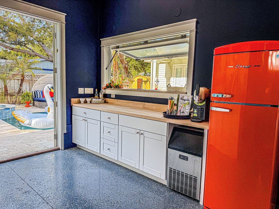 Flip-up bar window with retro fridge, extra storage, large ice maker, and plenty of space to mix drinks — perfect for poolside entertaining.