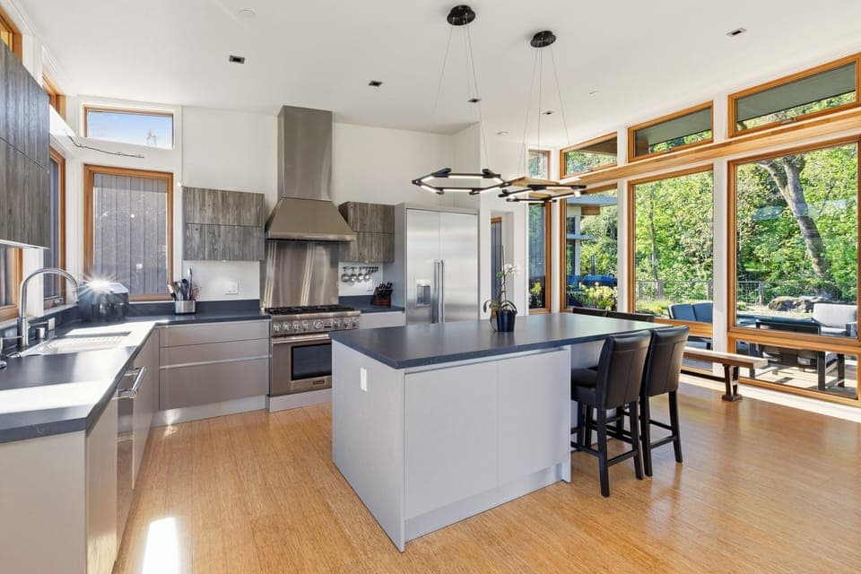 Your sleek modern kitchen features premium appliances and a spacious island, all bathed in natural light from floor-to-ceiling windows overlooking lush greenery.