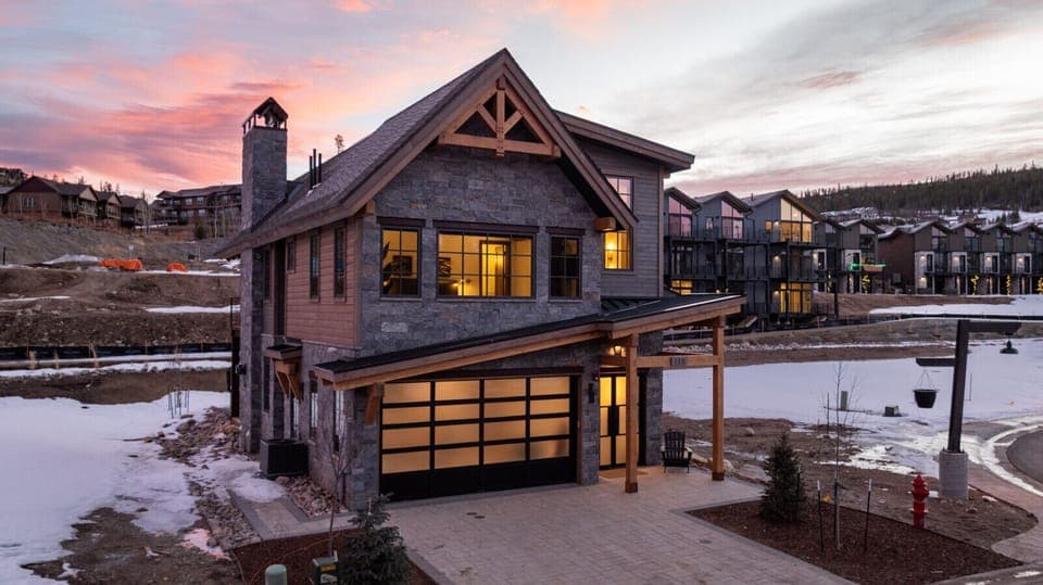 Home exterior at dusk with stone and wood siding, glass garage door, and glowing interior lights