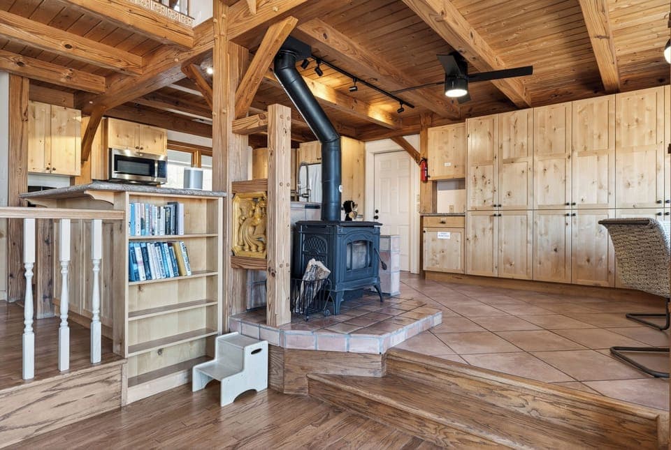 A warm, open-concept living space anchored by a wood-burning stove and rich timber beams—perfect for cozy nights in.