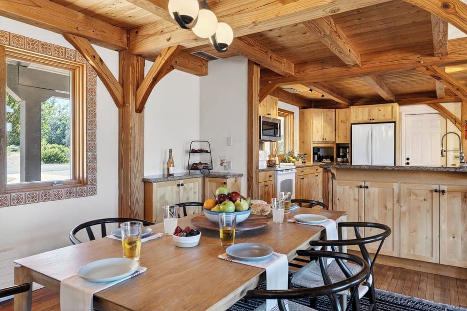 A warm, wood-beamed dining space perfect for gathering, with natural light pouring in and a table set for shared meals.