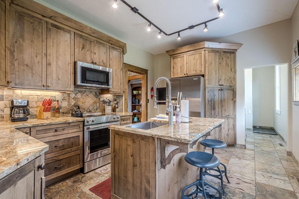 Granite countertops and natural wood cabinets surround stainless steel appliances in this kitchen with tiled floors.