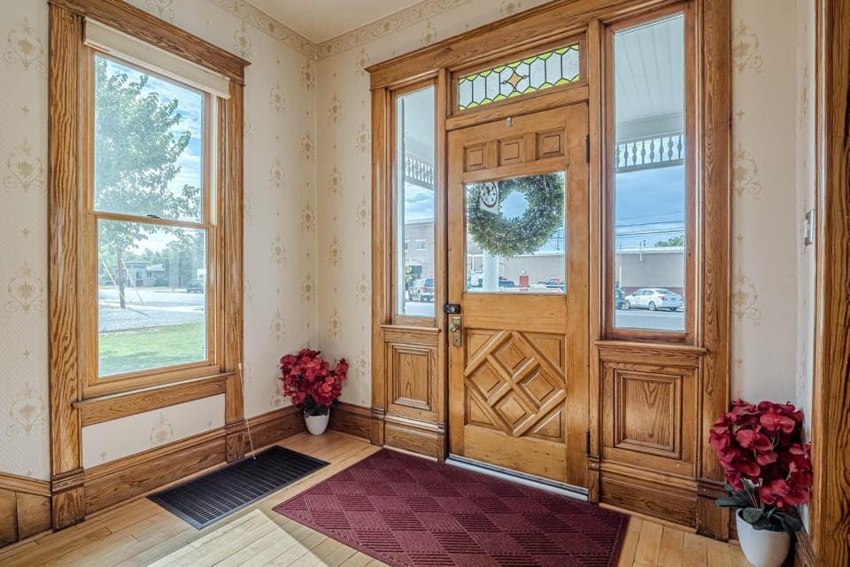 Entryway with natural wood door featuring diamond paneling, stained glass transom, and floral wallpapered walls.