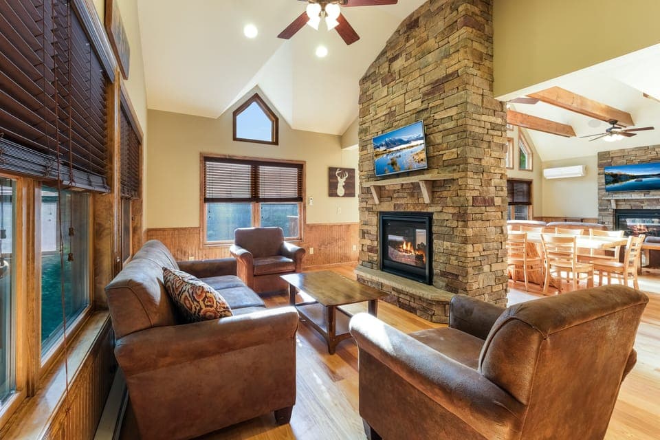 An angled photo of the fireplace of the great room behind the dining table, with seating and TV.
