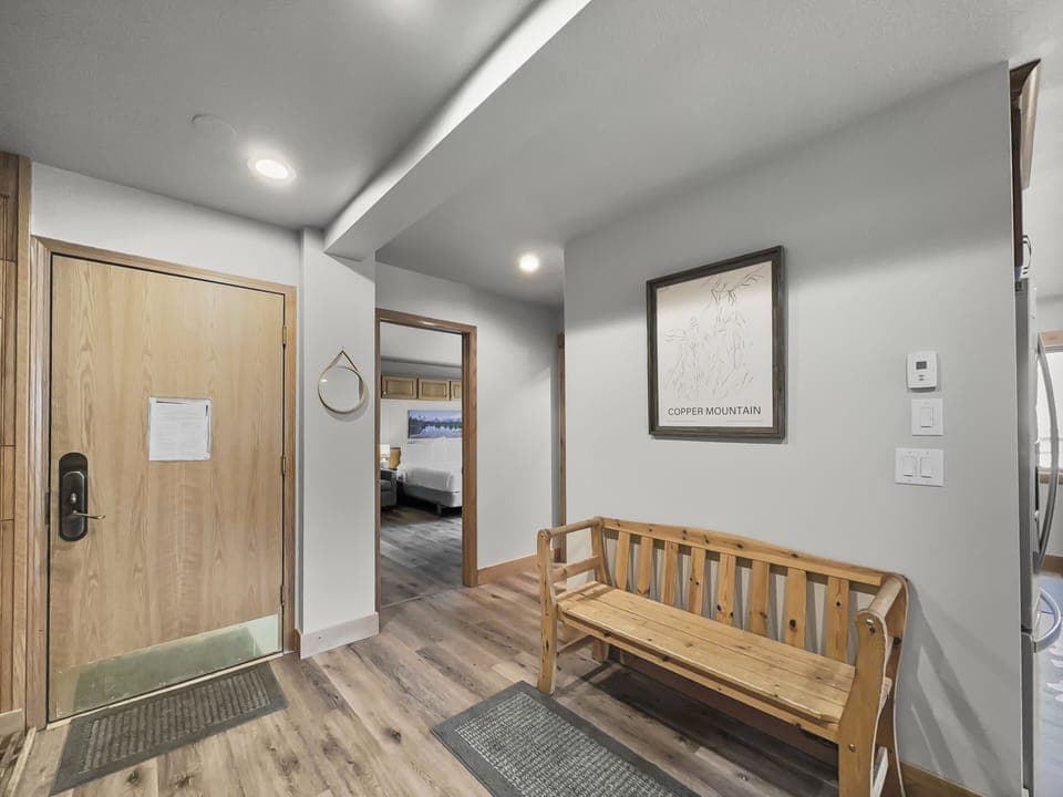 A hallway with a wooden bench, a wall-mounted picture marked "Copper Mountain," a door with a note, and visible adjoining rooms.
