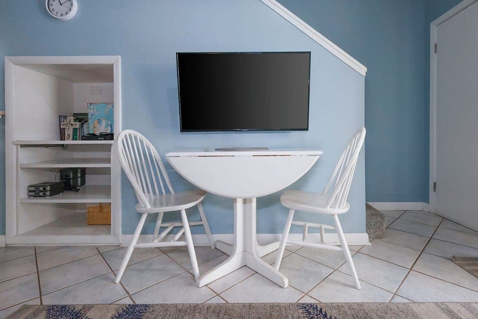 This cozy nook features a wall-mounted TV and a charming round table with two white chairs, perfect for meals or games