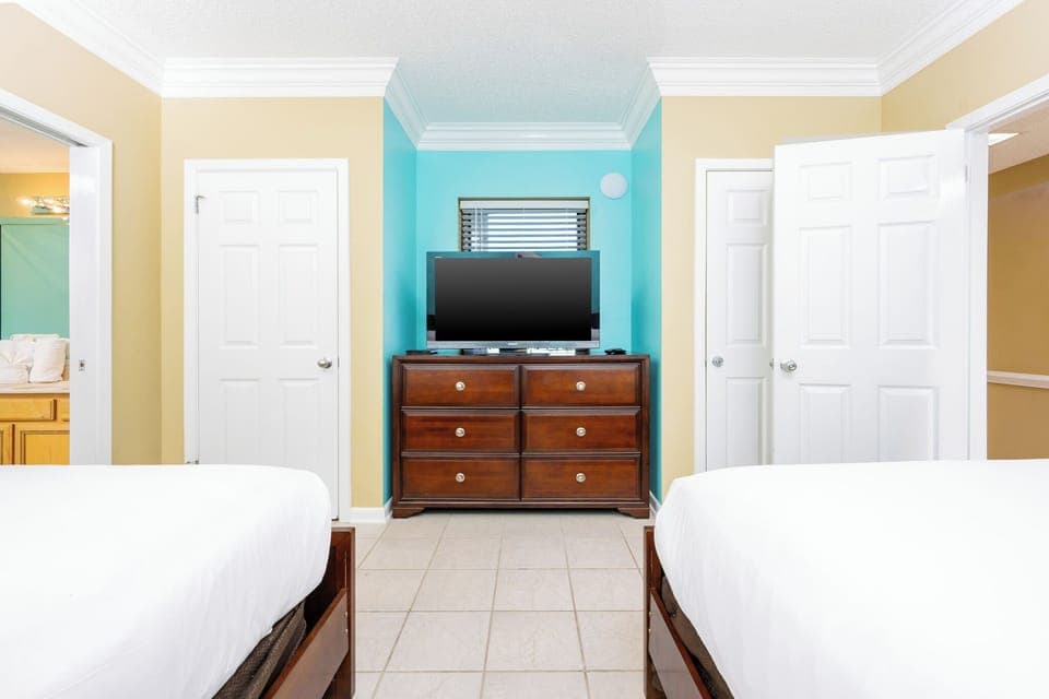 This guest bedroom features two queen beds, a dresser with a flat-screen TV, and colorful walls that create a cheerful vibe
