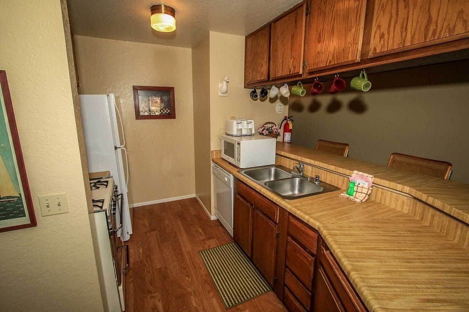 A view of the kitchen's layout highlighting the double sink and microwave. The wood-toned cabinetry and practical flooring make for a clean and efficient space for all your culinary needs.