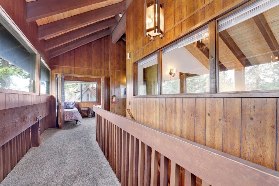 This bright hallway features classic wood-paneled walls and vaulted ceilings. Large windows overlook the living area below, while the plush carpeting leads to the comfortable private bedrooms.