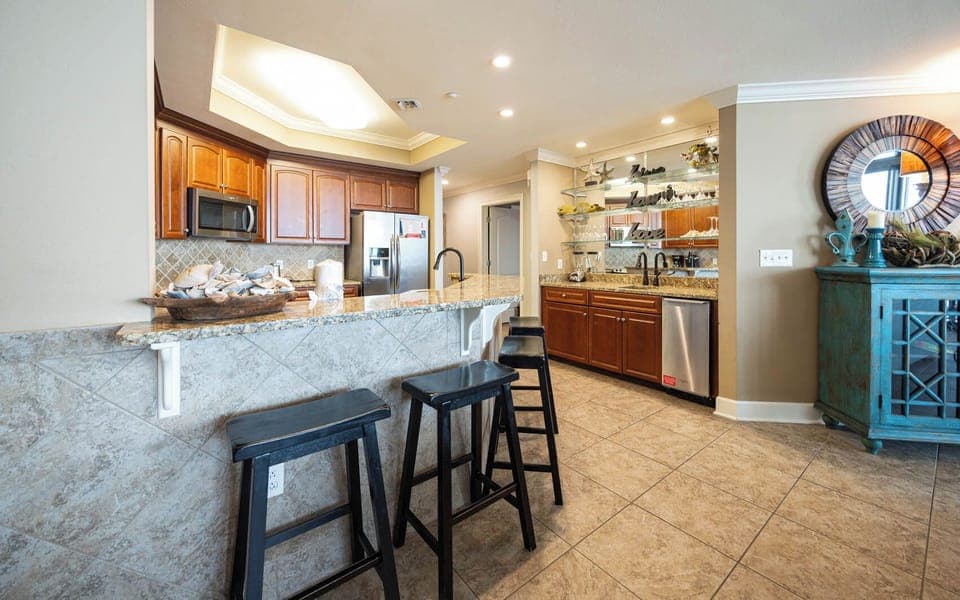 The kitchen features wooden cabinetry, granite countertops, and a cozy bar area with black stools, perfect for casual dining