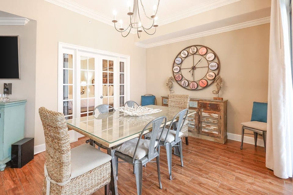 This dining area features a stylish glass table, woven chairs, a large wall clock, and a cozy ambiance perfect for gatherings