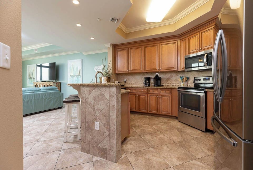 The kitchen features stainless appliances, granite countertops, and a view into the inviting living area with a TV