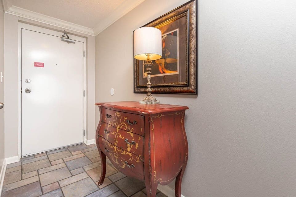 Step into a welcoming entryway featuring a decorative chest, elegant lamp, and framed artwork to set a warm tone
