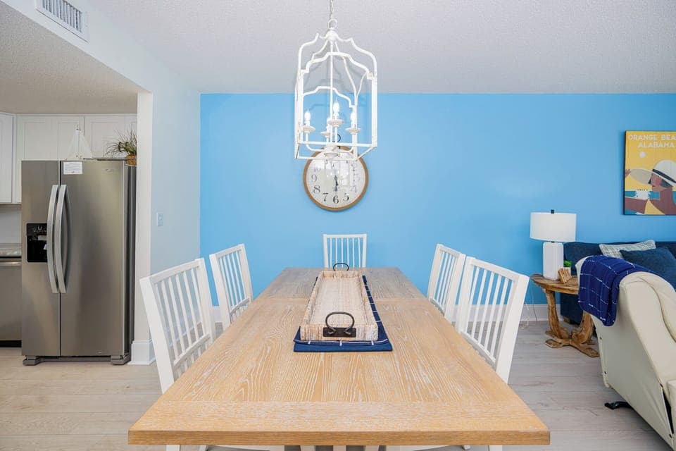 Gather around the light wood dining table with white chairs, set against a cheerful blue wall and stylish decor