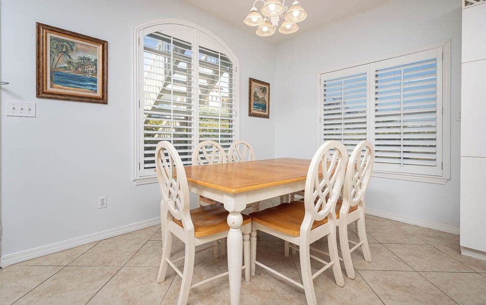 The dining area features a light wood table surrounded by six chairs, with bright natural light streaming through the window