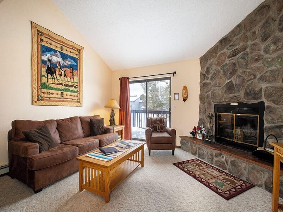 Cozy up in your mountain retreat with plush seating, stone fireplace warmth, and peaceful balcony views of snowy peaks.