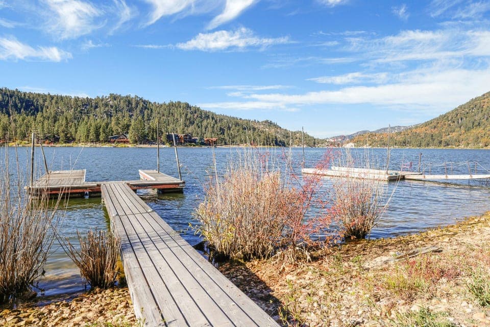 A wooden dock extends into a calm, blue lake, surrounded by lush, pine-covered mountains under a wispy sky. This serene setting offers a quiet escape and a front-row seat to the beauty of nature.