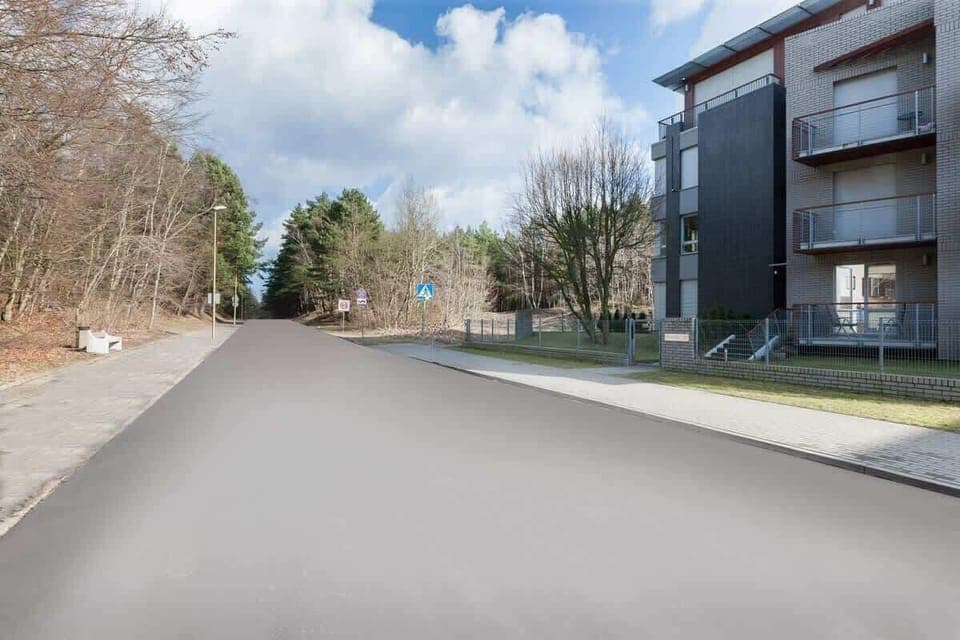 A quiet residential street with modern apartment buildings on either side. Trees and open spaces add a touch of nature.