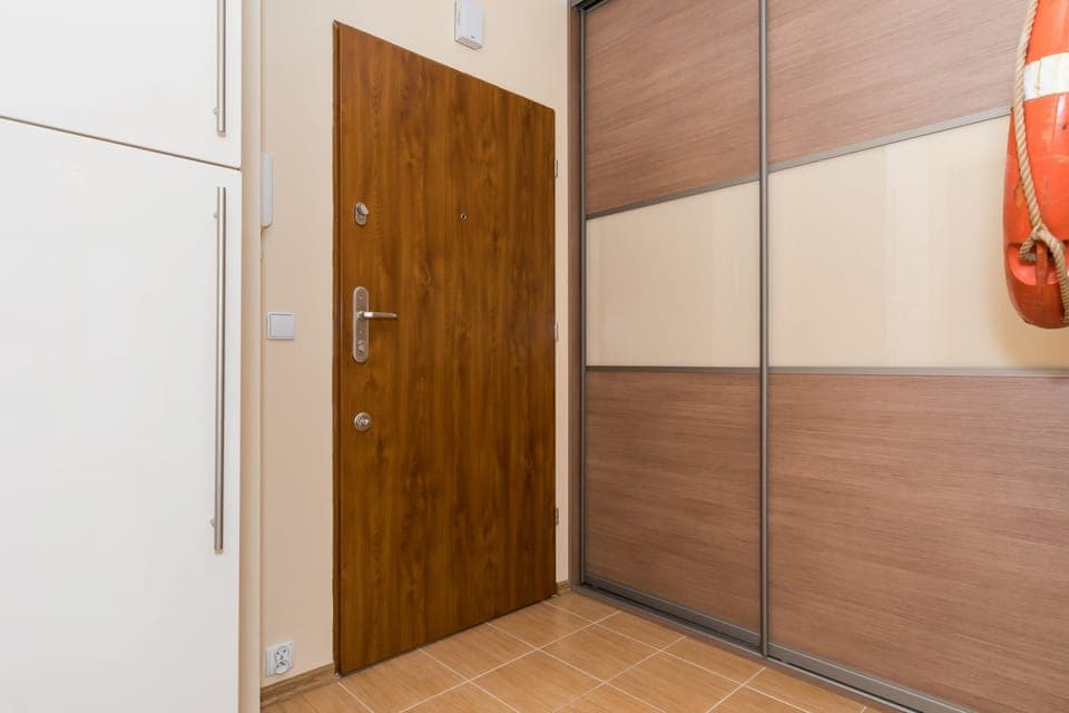 A view of the apartment’s front door, showing a wooden finish with modern design elements. The area is simple and functional.