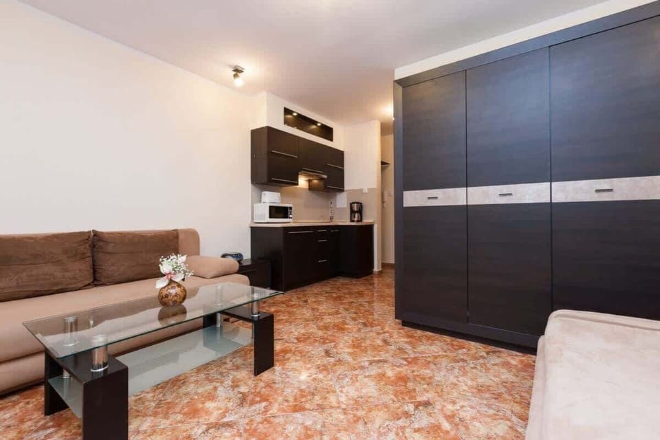 A similar view as the previous one, showing the couch and bed in the same shared space. There is a large wardrobe in dark wood, adding plenty of storage.