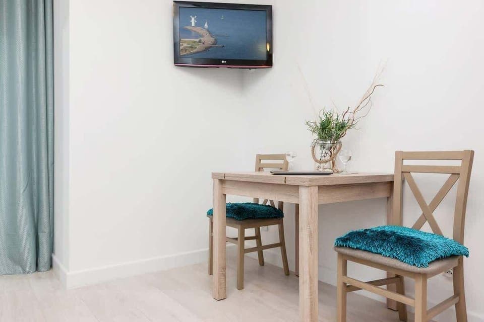 Another view of the same small table and chair setup from image 3, this time taken from a different angle. The TV on the wall and the blue curtains add to the room's simple and serene atmosphere.