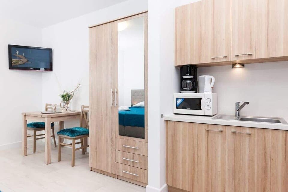 The kitchenette is compact and modern, featuring light wooden cabinets, a countertop, and essential appliances like a stove and coffee maker. It’s functional and seamlessly integrated into the living space.