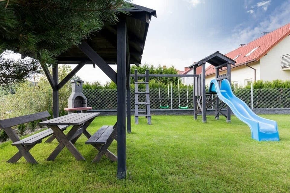 An outdoor area with a wooden gazebo, a picnic table, and a playground set, perfect for family gatherings and outdoor play.