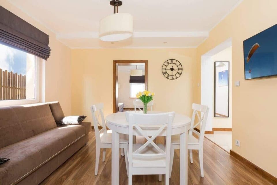 Dining area with white table with round top and fold-out sofa. To the right, a painting with a paraglider hangs on the wall. 