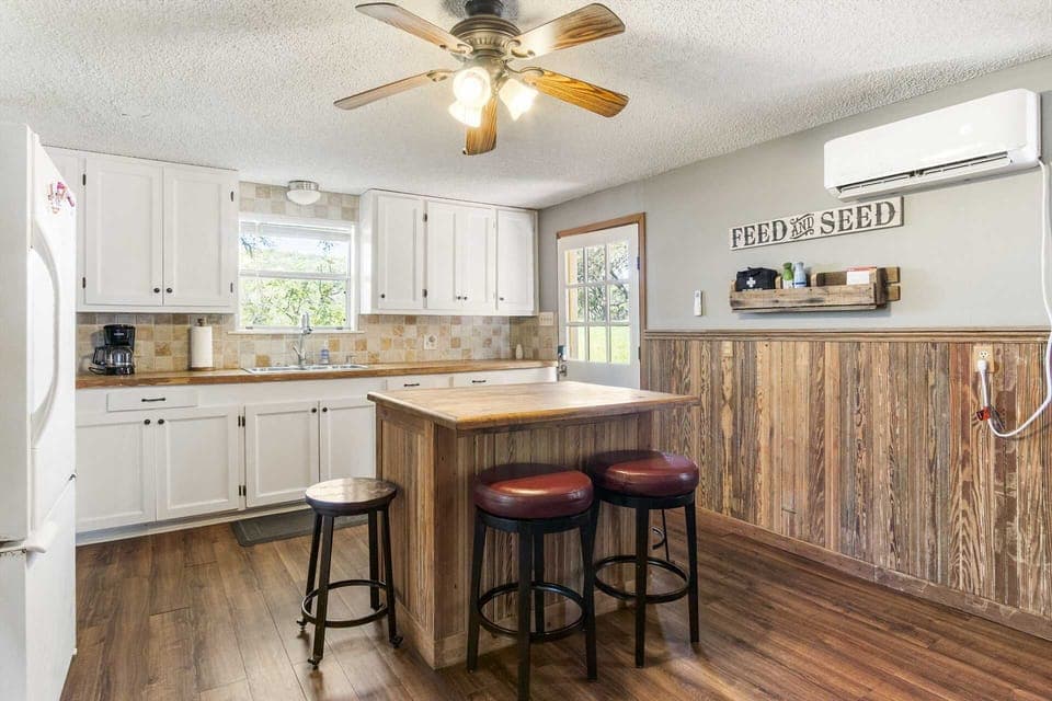 Bright country kitchen with modern charm, featuring a butcher-block island, cozy bar stools, and garden views.