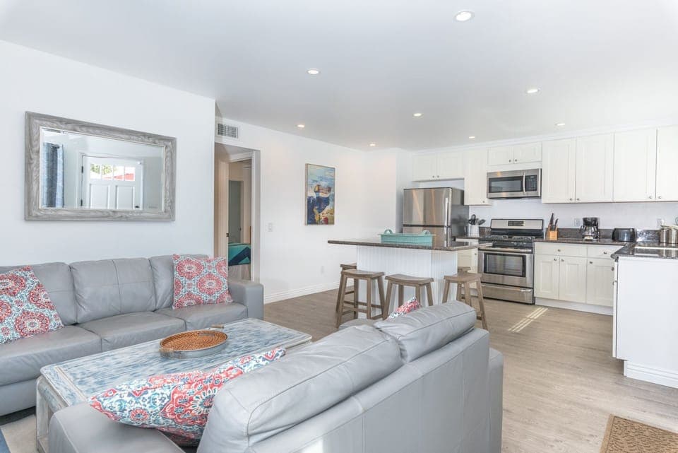 Front door opens up to the main living area, with a sofa set, cable TV, and open kitchen area.
                