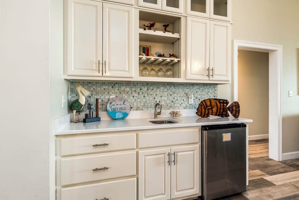Your kitchen features white cabinetry, mosaic backsplash, and wine storage—perfect for preparing meals and beach-themed entertaining.