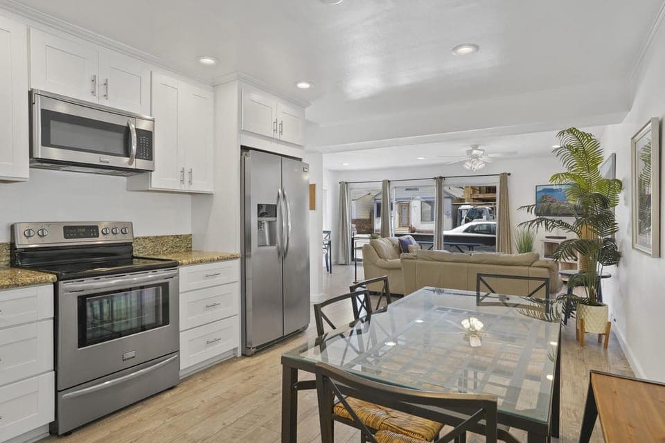 Vantage point from dining table and seating toward kitchen, living room and TV. Wood-look laminate flooring throughout.
                