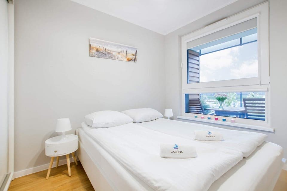 A bedroom with a neatly made bed, white bedding, and minimalist decor, creating a peaceful and relaxing ambiance.