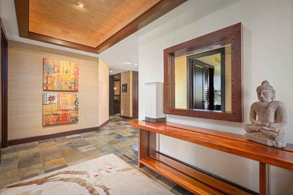 A curated entryway featuring warm textures, original art, and a mirror reflecting Hualalai elegance.