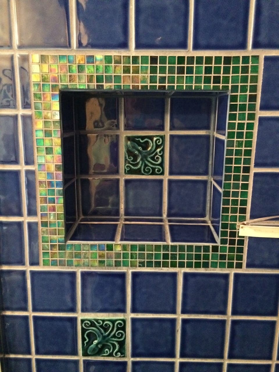 Recessed shelf in walk-in custom tile shower adorned with whimsical octopus tile
