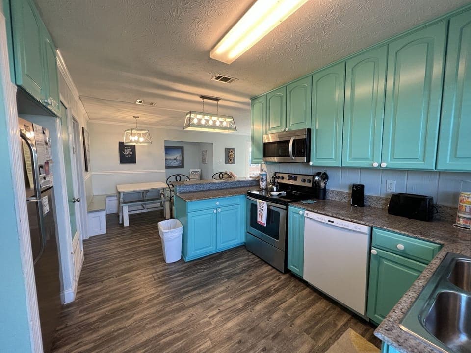Your fully-equipped kitchen awaits with turquoise cabinets, granite counters, and stainless steel appliances—perfect for creating memorable meals during your stay.