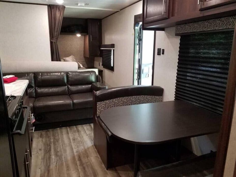 Inside view of Camper B featuring dinette table, sleeper sofa, queen bed in back and kitchen. 