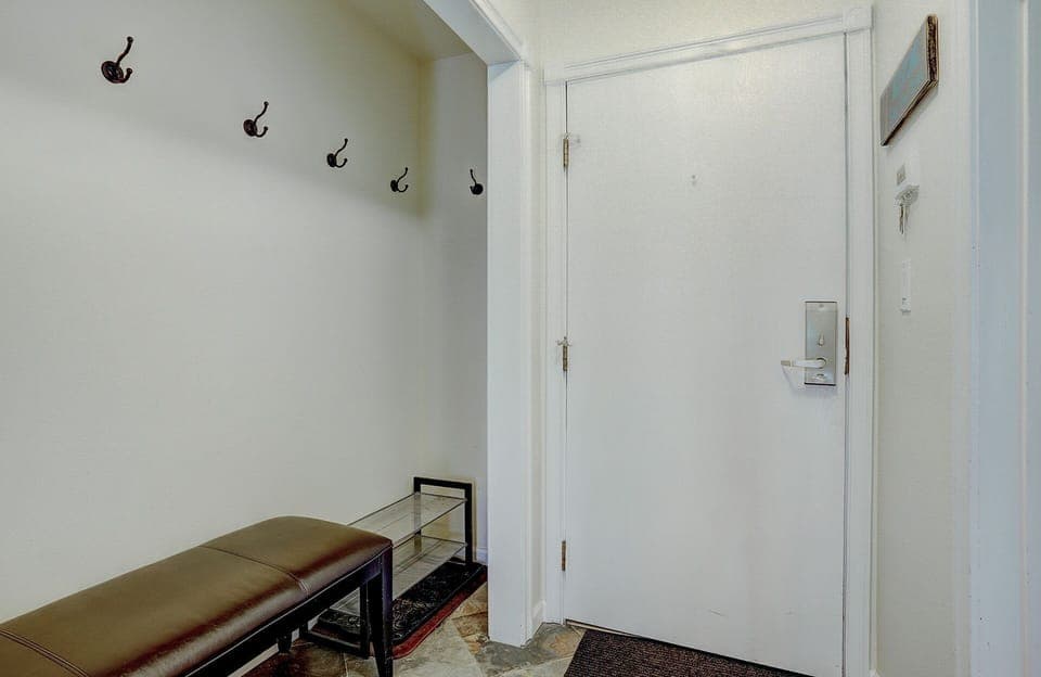 A small entryway with a bench, coat hooks on the wall, a glass table, and a white front door.