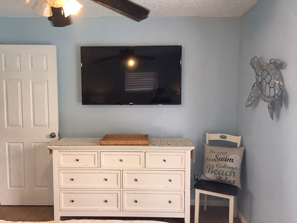 Large flat screen, sea turtle art work, dresser and chair master bedroom