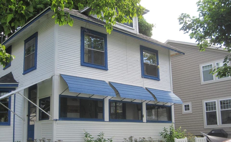 Bedrooms upstairs, porch downstairs, chairs, hammock, rockers on lakefront lawn.