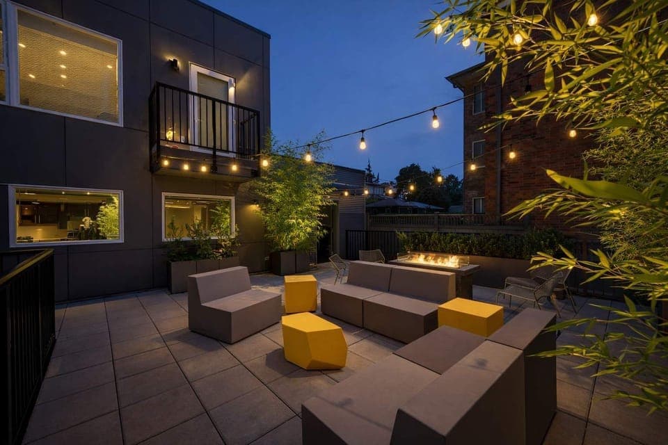 Modern outdoor lounge with cozy seating, string lights, and lush greenery—perfect for evening relaxation and social gatherings.
