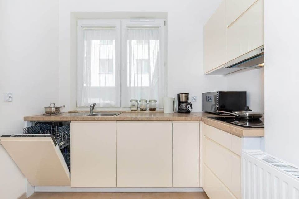 Functional and beige kitchen with a microwave, a dishwasher, a coffee maker, a toaster, and a kettle.