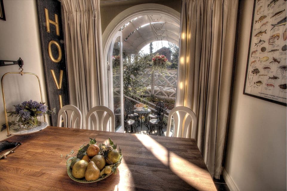 Doors open onto a walled furnished patio with rose-covered ornate pergola
