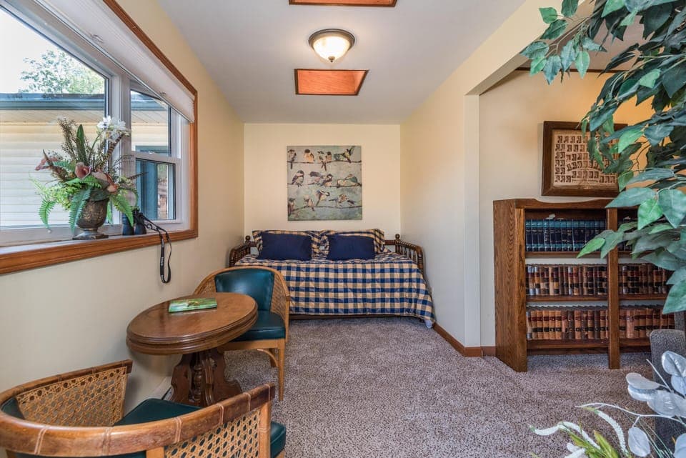Small sitting area with round wooden table, cane-back chairs, and a daybed covered in blue plaid bedding.